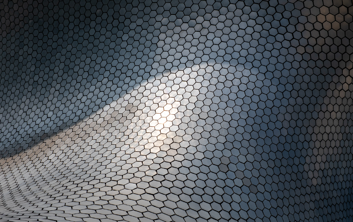 Abstract close-up of a hexagonal mesh surface forming a smooth wave, with a bright light spot in the center.
